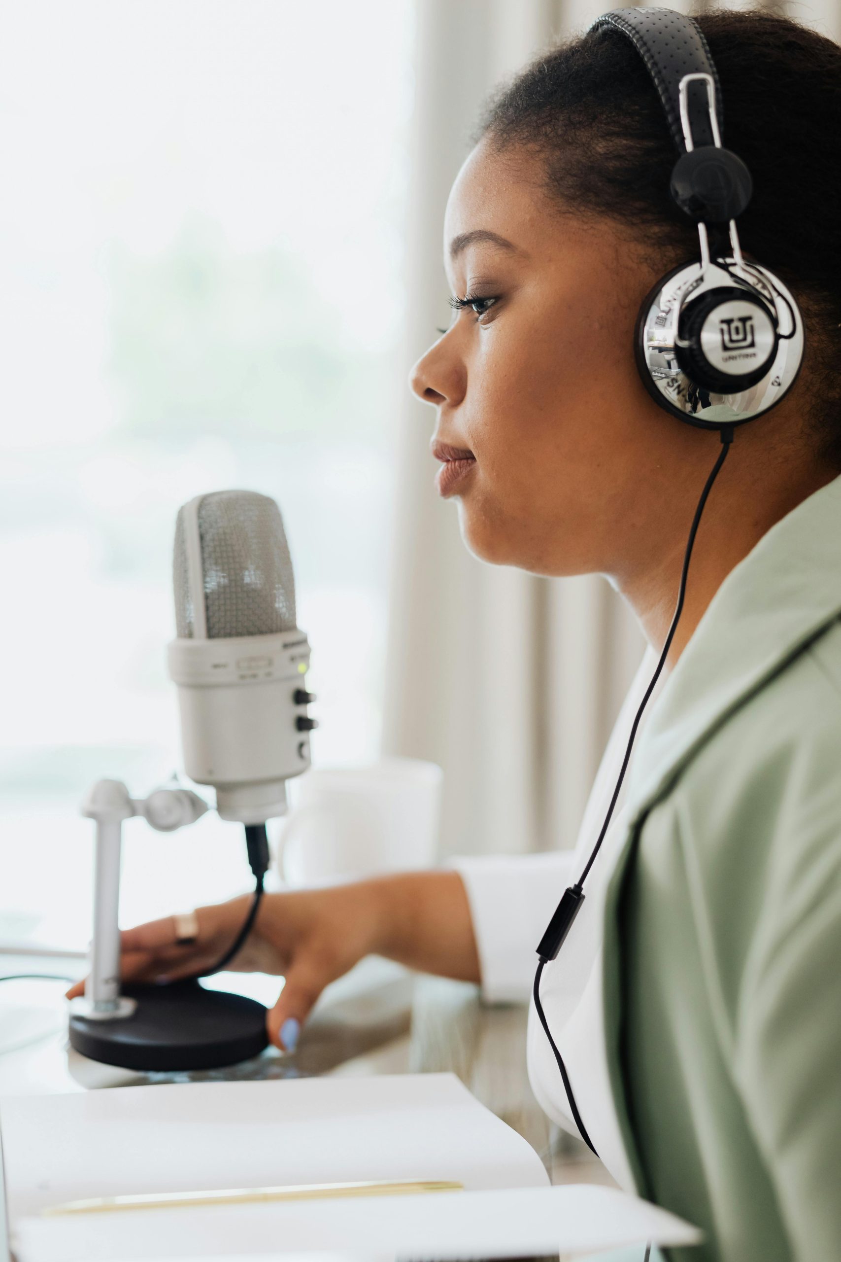 Side view of a woman recording a podcast with a condenser microphone and headphones.